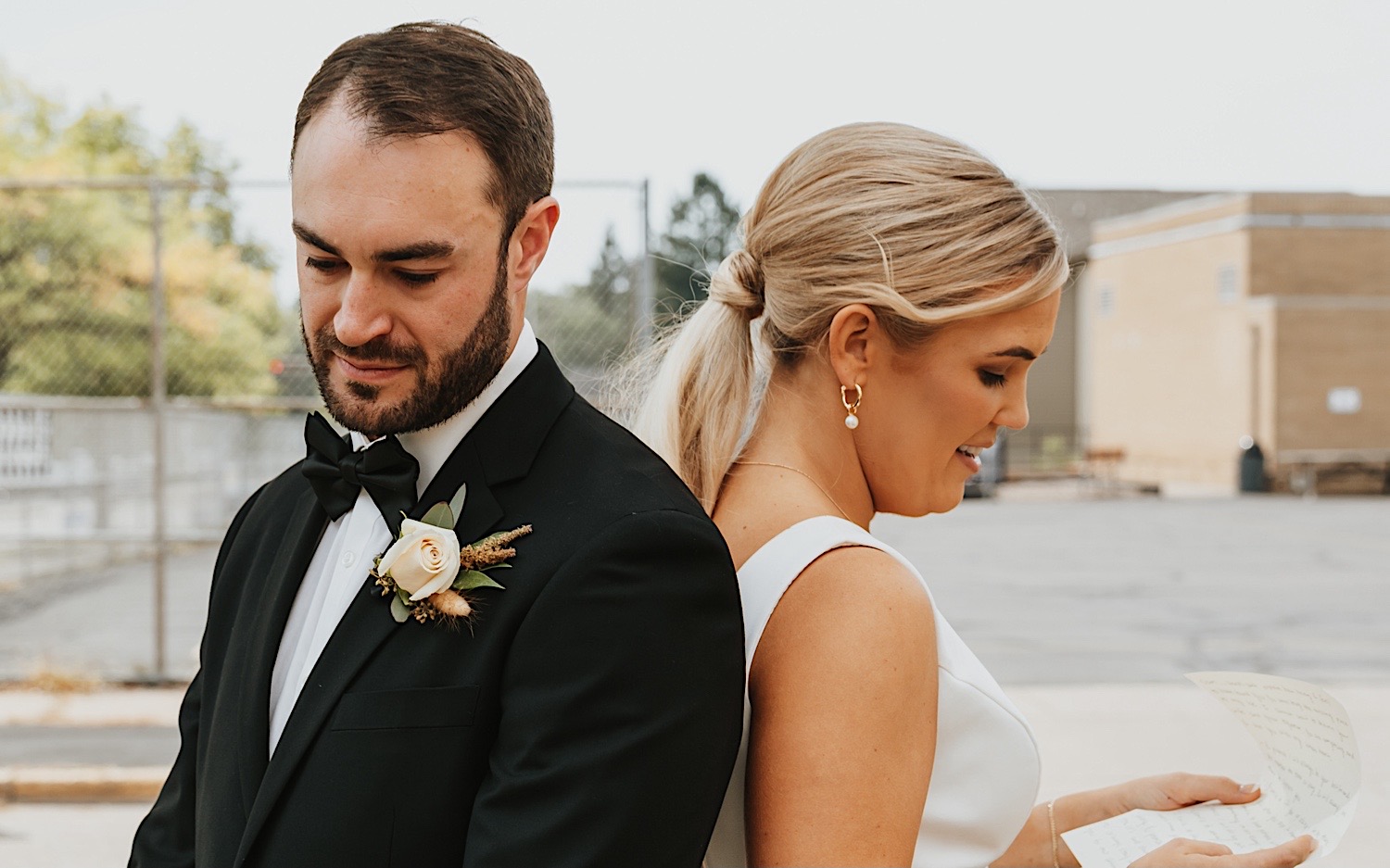 A bride and groom stand back to back reading their vows to one another before their first look