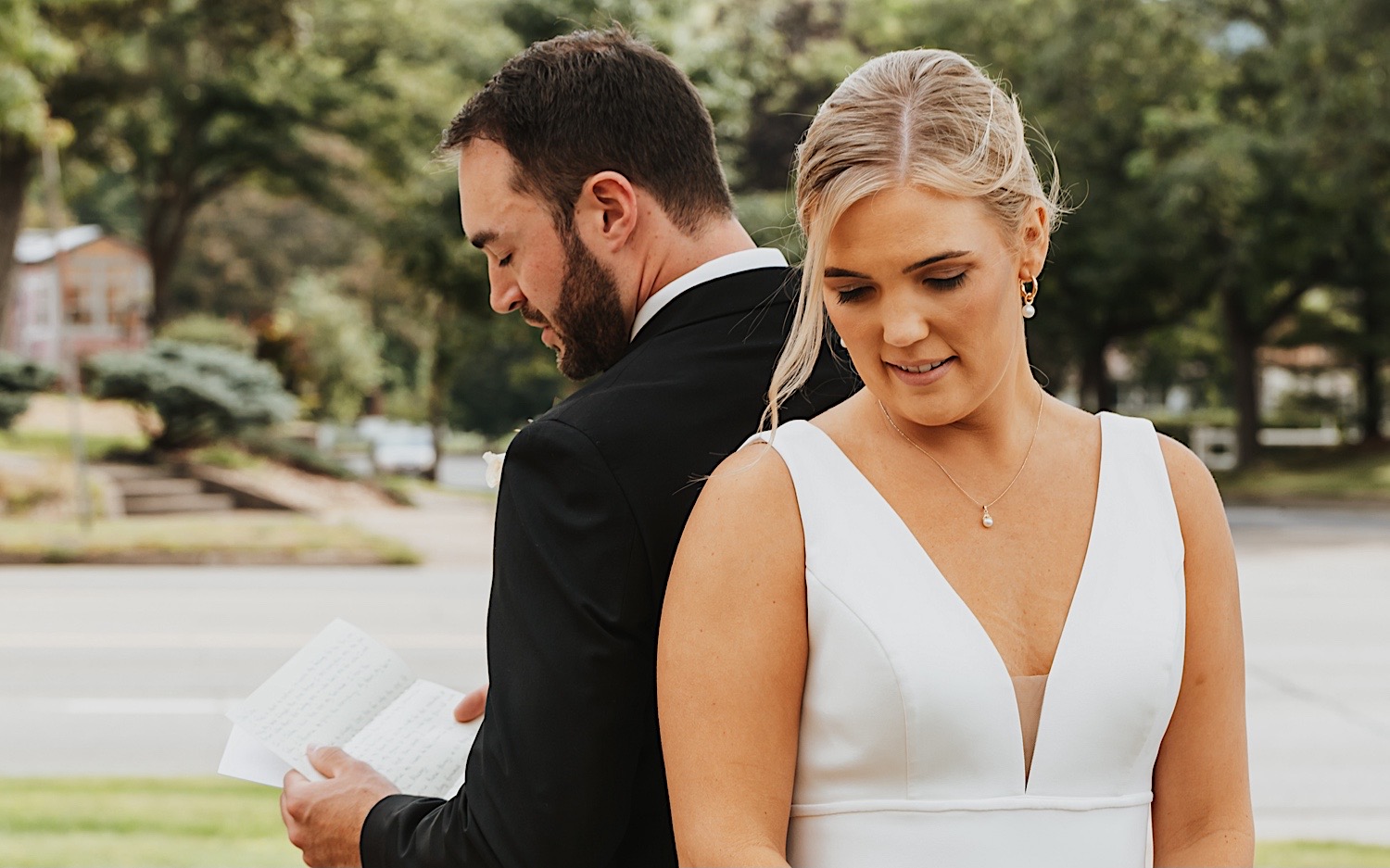 A bride and groom stand back to back as the groom reads his vows