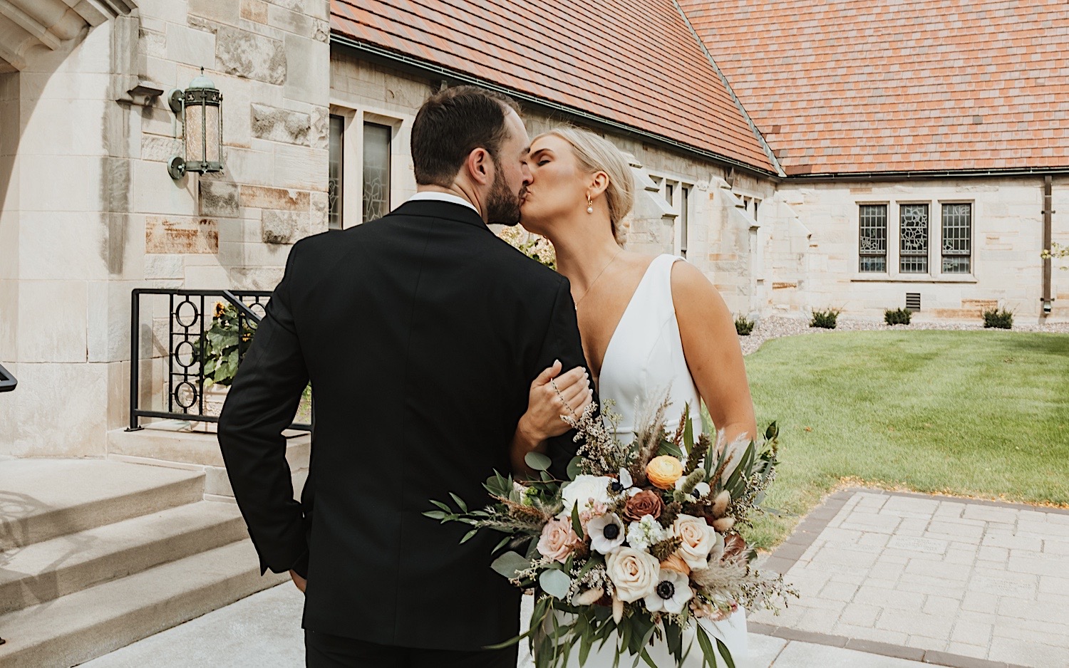 A bride and groom lock arms and kiss one another