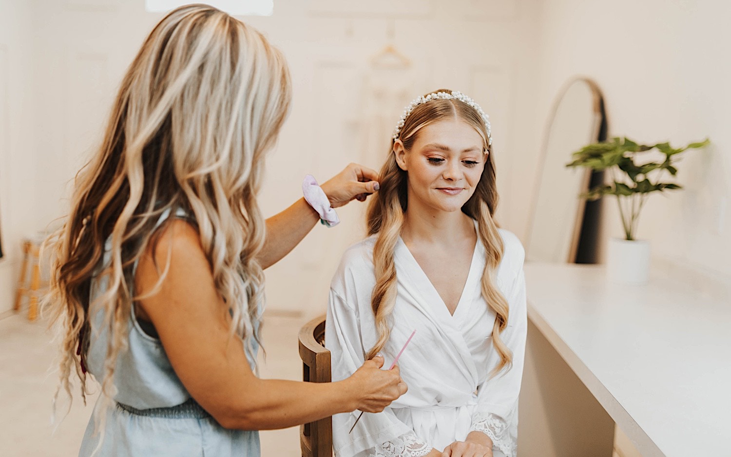 A bride sits in a chair as a woman works on her hair to get her ready for her wedding day at The Aisling