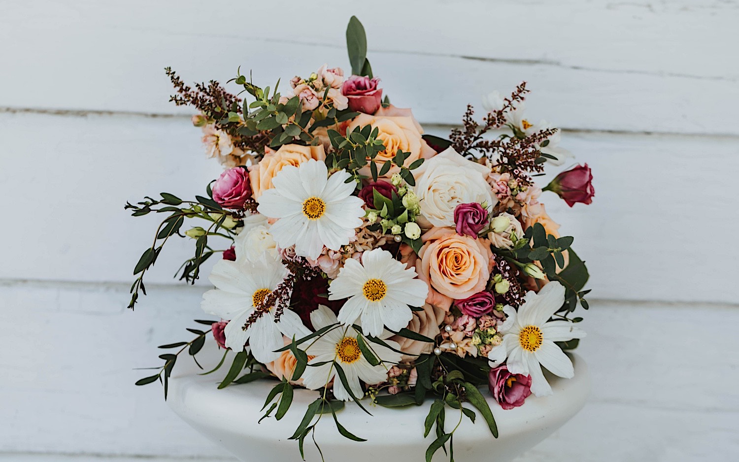 A flower bouquet rests on a small table outside of a white building