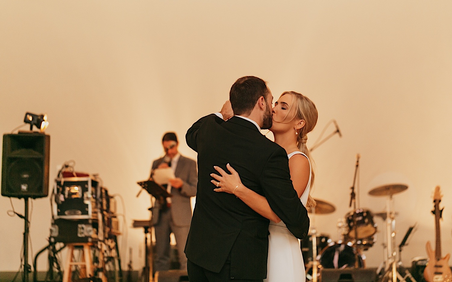 A bride and groom kiss during their first dance at their wedding reception in the La Crosse Center while the live band plays behind them