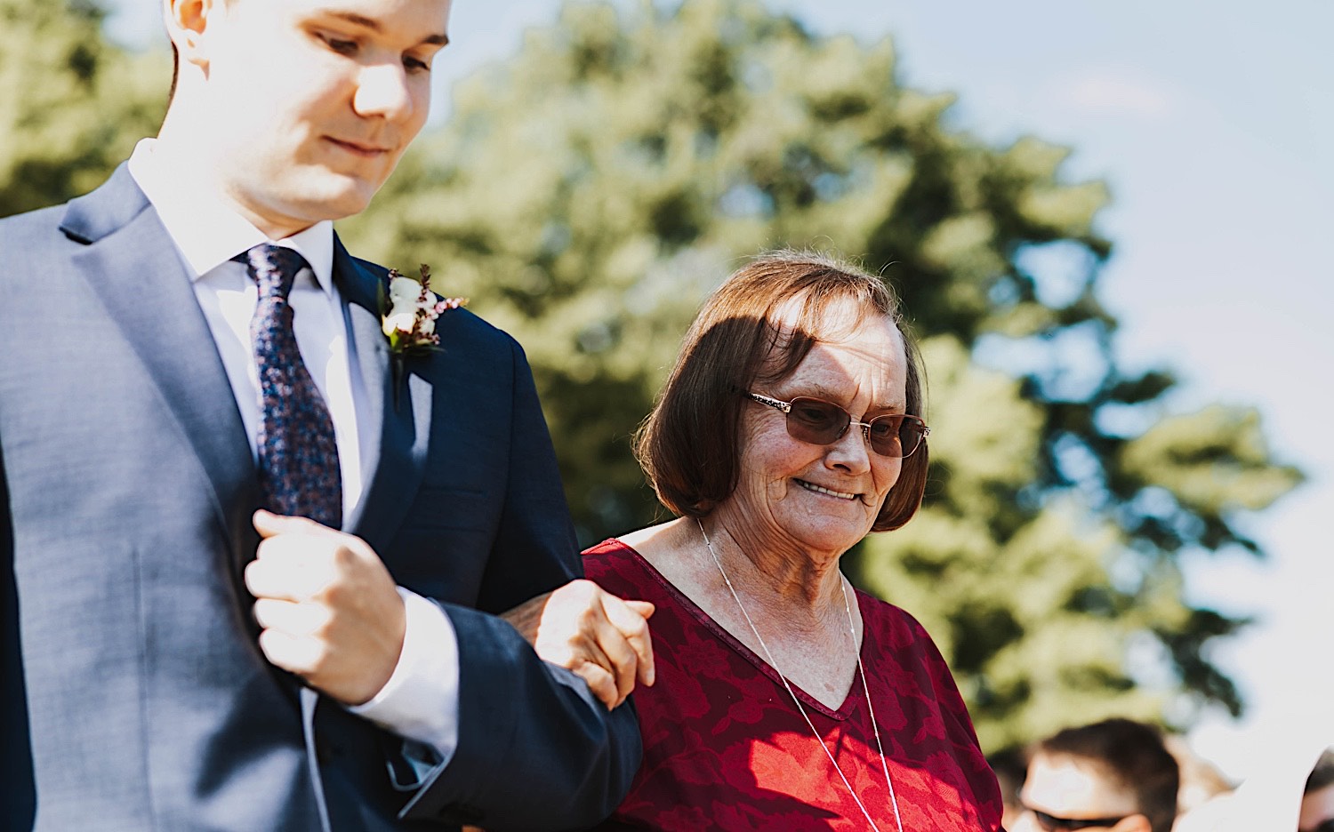 A woman smiles while being walked down the aisle of a wedding ceremony by a man