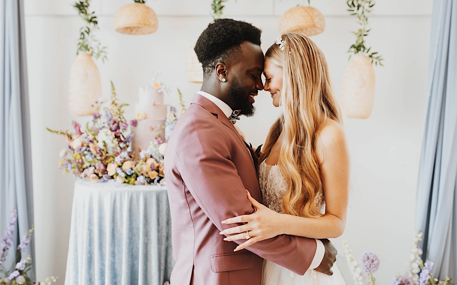 A bride and groom smile as they touch foreheads together while standing in front of their wedding cake during their reception at The Aisling