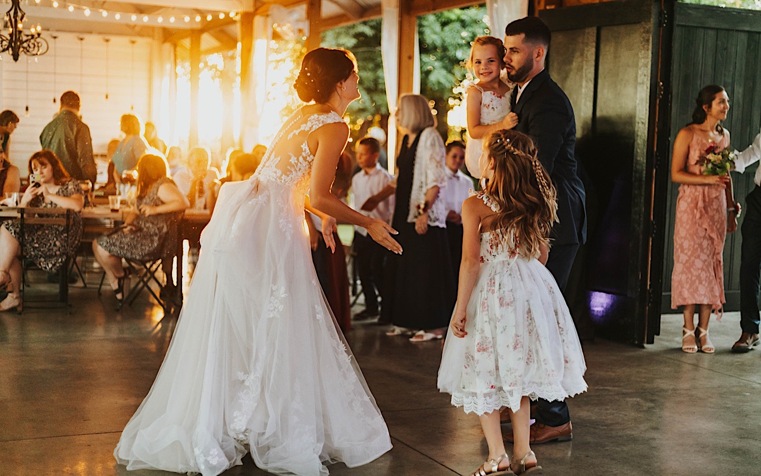 A bride and groom dance with two of their flower girls during their wedding reception at Legacy Hill Farm as the sun sets behind them